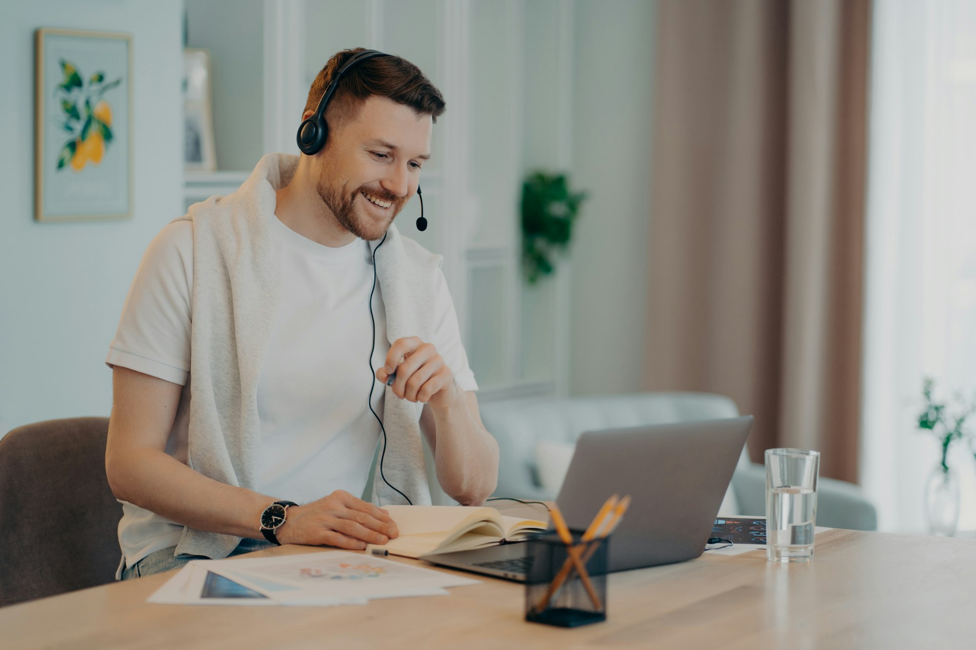 Happy man enjoying learning at home and using headset and laptop